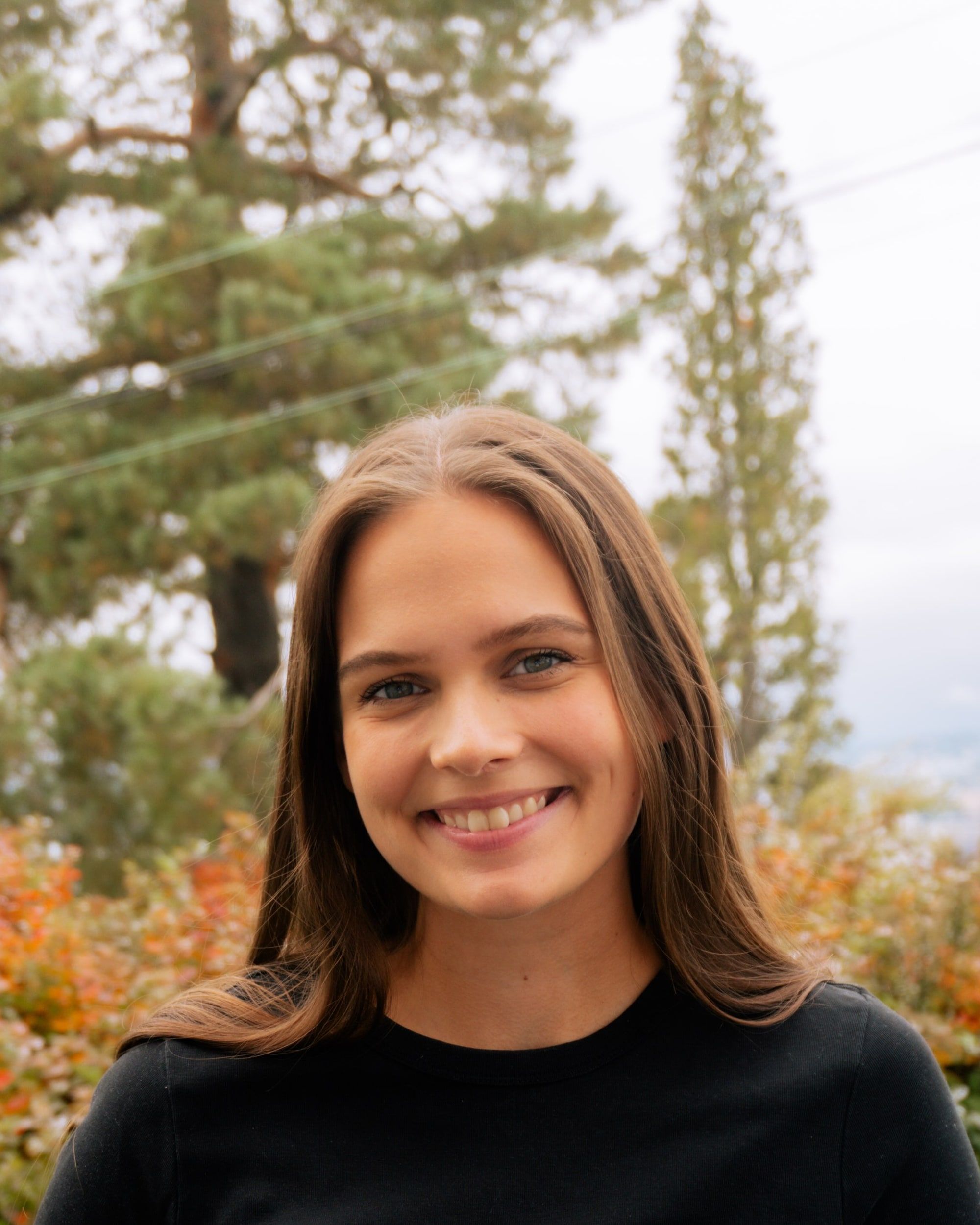 Portrett av Veronika Flø som smiler, med høstfarger og trær i bakgrunnen