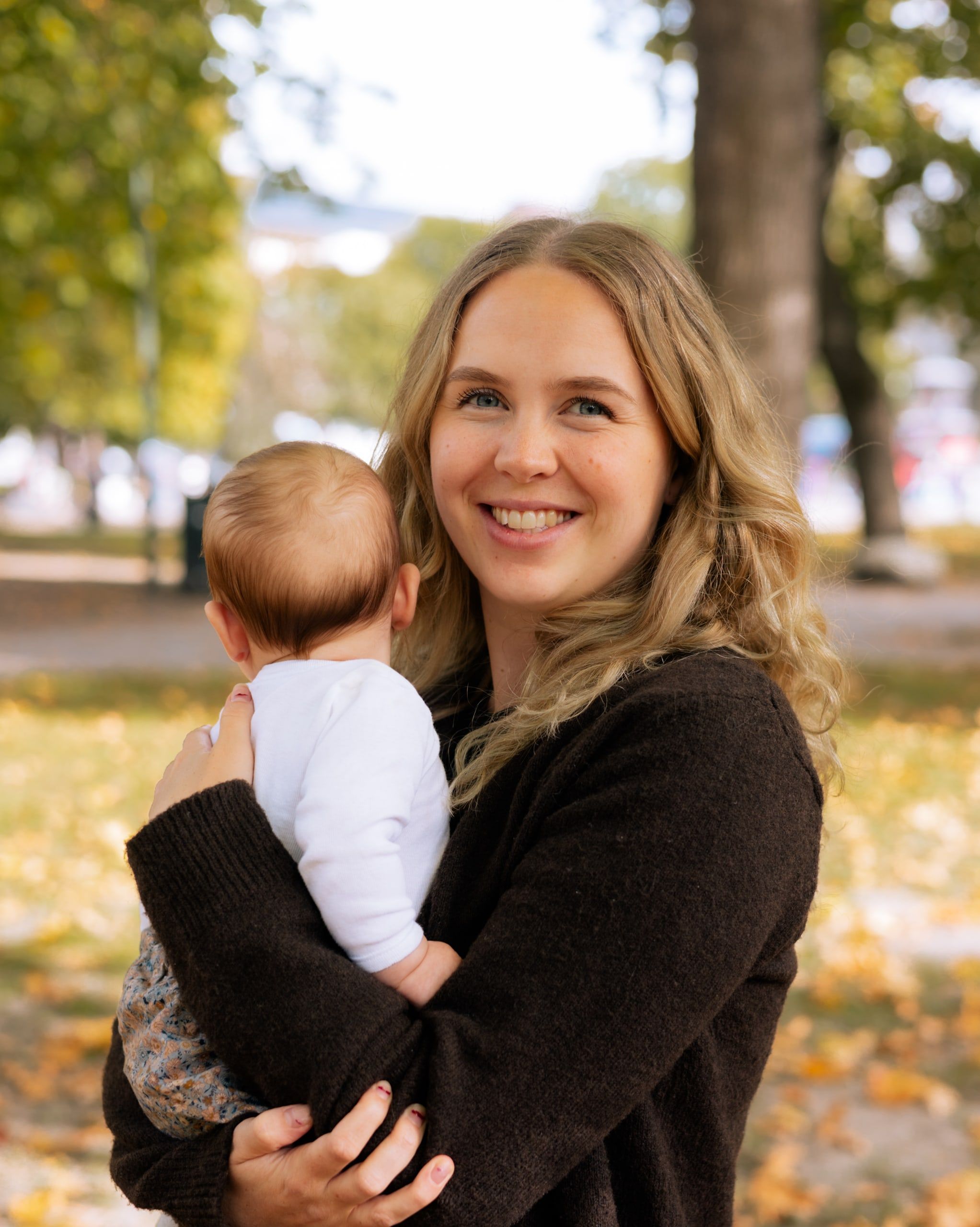 Smilende kvinne holder en baby i en høstfarget park